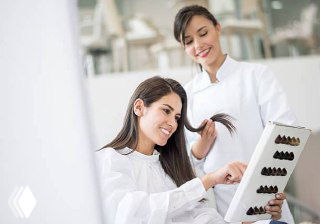 Стилист в салоне показывает клиентке палитру оттенков волос, клиентка улыбается — иллюстрация взаимодействия и выбора услуги в салоне.