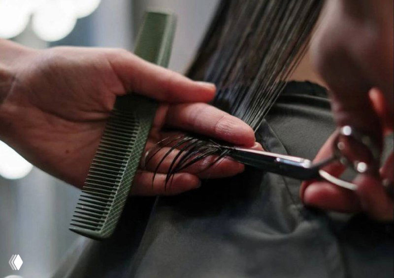 Рука мастера с расчёской и ножницами подстригает волосы клиента в салоне — иллюстрация к статье о мотивации мастеров KPI.bi