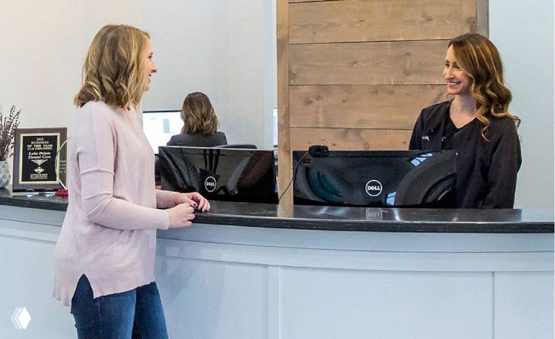 Администратор у стойки ресепшн общается с клиенткой; видны стойка и монитор — иллюстрация внимательного клиентского сервиса.