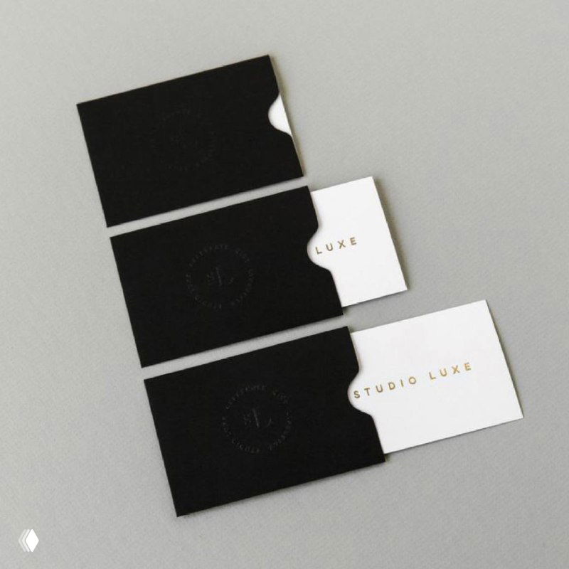 Черно-белые визитки, аккуратно выложенные на светло-сером фоне; видны тиснение и золотистая печать, минималистичный фирменный стиль.