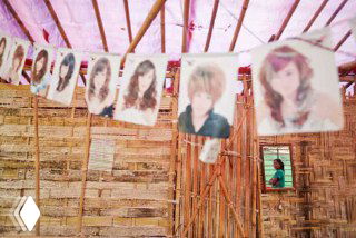 Фотографии причёсок висят в стенде парикмахерской в небольшой французской витрине; видно элементы местной уличной сцены.