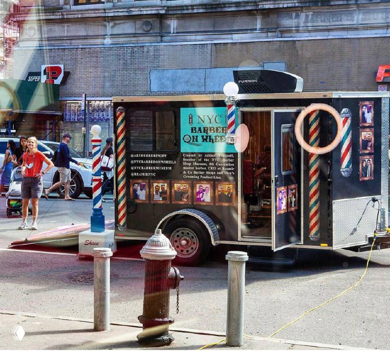 Фотография передвижной парикмахерской NYC Barber on Wheels на городском тротуаре с характерной вывеской, декором и полосатыми столбами.