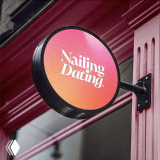 Круглая вывеска с надписью «Nailing Dating» на фасаде салона — заметный логотип и оформление витрины на фоне городского фасада в Лондоне.