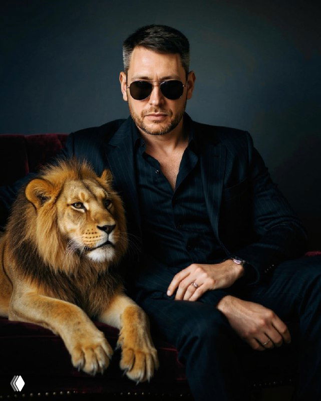 Мужчина в тёмном костюме рядом с львом — стилизованный кинематографичный портрет, подчёркивающий силу и композицию кадра.