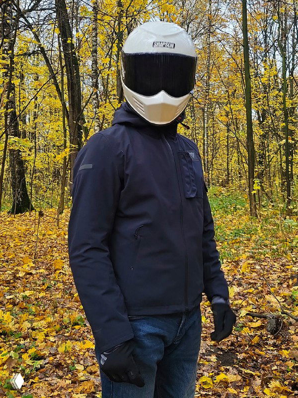 Человек в тёмно-синей непромокаемой куртке Dainese и белом шлеме на фоне осеннего леса, вид в фас — демонстрация посадки и кроя куртки.