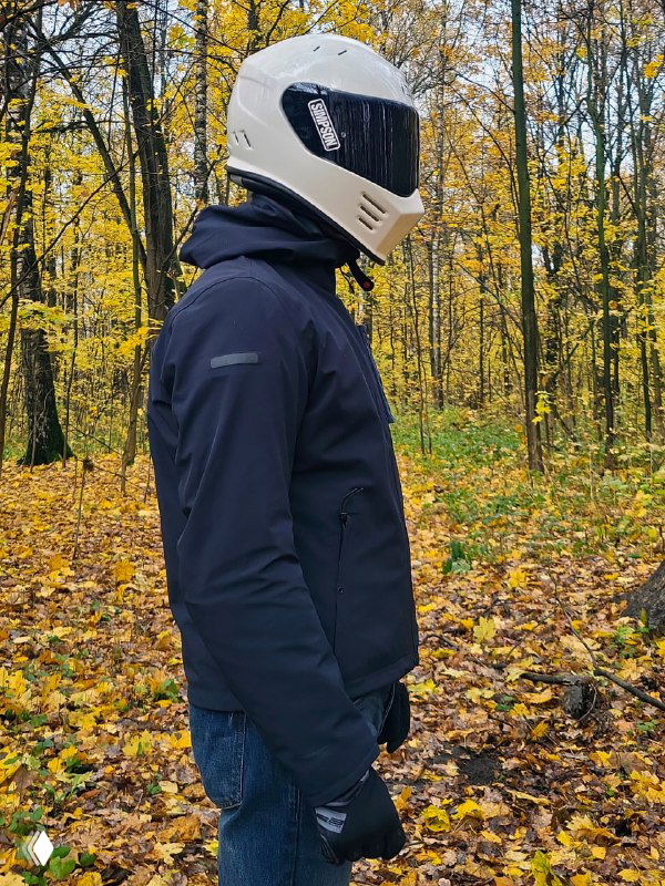 Боковой профиль куртки Dainese Corso AbsØluteshell Pro: капюшон, рукав и посадка на мотоциклисте на фоне жёлтой осенней листвы.