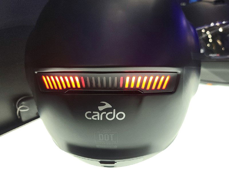 Задняя часть шлема Cardo с яркой светодиодной панелью стоп-сигнала и логотипом Cardo на матовой поверхности корпуса, крупный план.