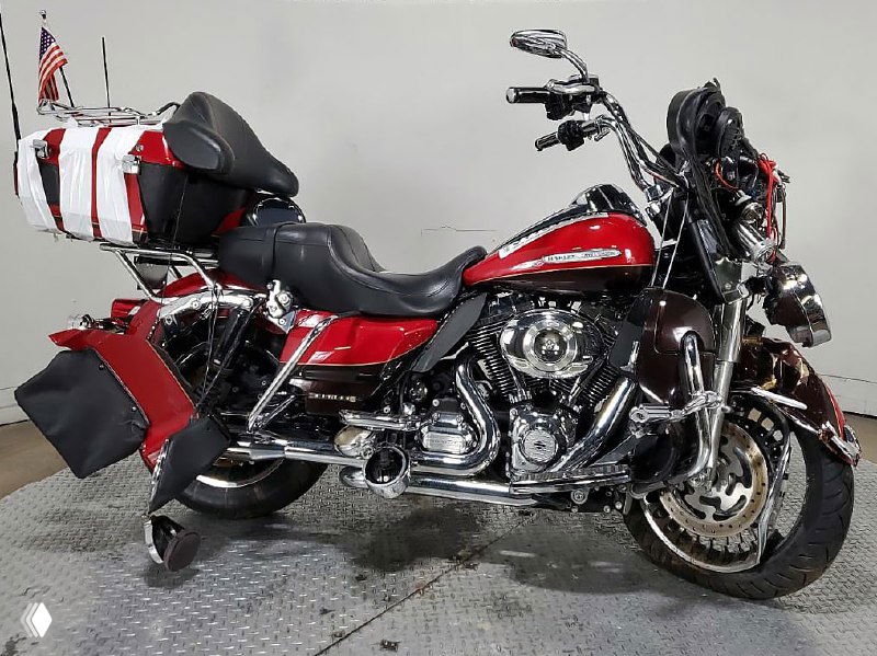 Красный Harley-Davidson в боковом ракурсе с багажником и упакованным тентом, внутри помещения — фото восстановленного или кастомизированного мотоцикла.