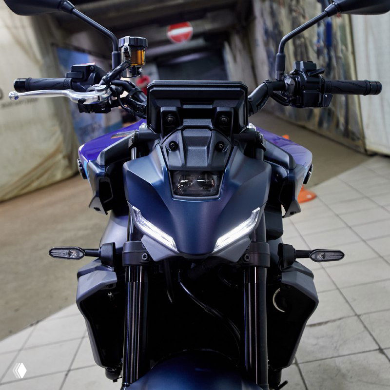 Фронтальный крупный план Yamaha MT-09 Y‑AMT в гараже: руль, приборная панель и светодиодные фары на фоне закрытого помещения.