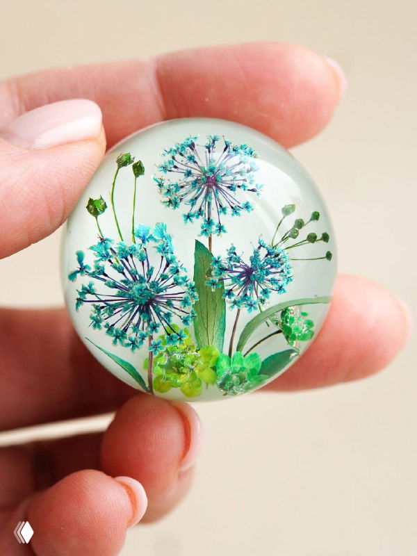 Рукотворная круглая подвеска с засушенными мелкими зонтичными цветами в прозрачной смоле, детализация цвета и фактуры.