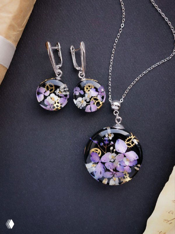 Комплект из серёжек и кулона с бледно-лиловыми высушенными гортензиями в прозрачной смоле, аккуратно выложенный на тёмном фоне для демонстрации комплектности.
