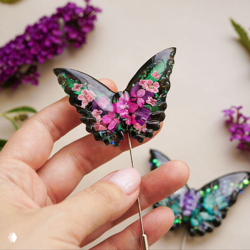 Макрофотография броши‑бабочки из эпоксидной смолы с мелкими розовыми цветами алиссума, детальное кадрирование в руках автора