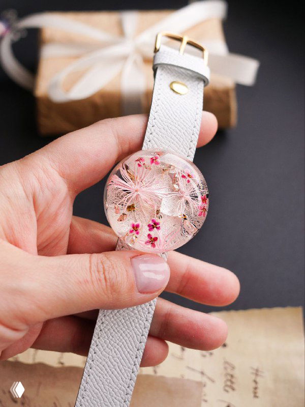 Ремешок с круглым кулоном из смолы, внутри просматриваются мелкие цветы и текстуры, крупный план руки держит изделие