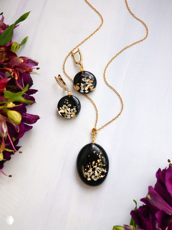 Набор подвесок и серёжек на тёмном фоне с золотистой фурнитурой, в смоле разбросаны сухие цветы и кусочки алиссума для текстуры