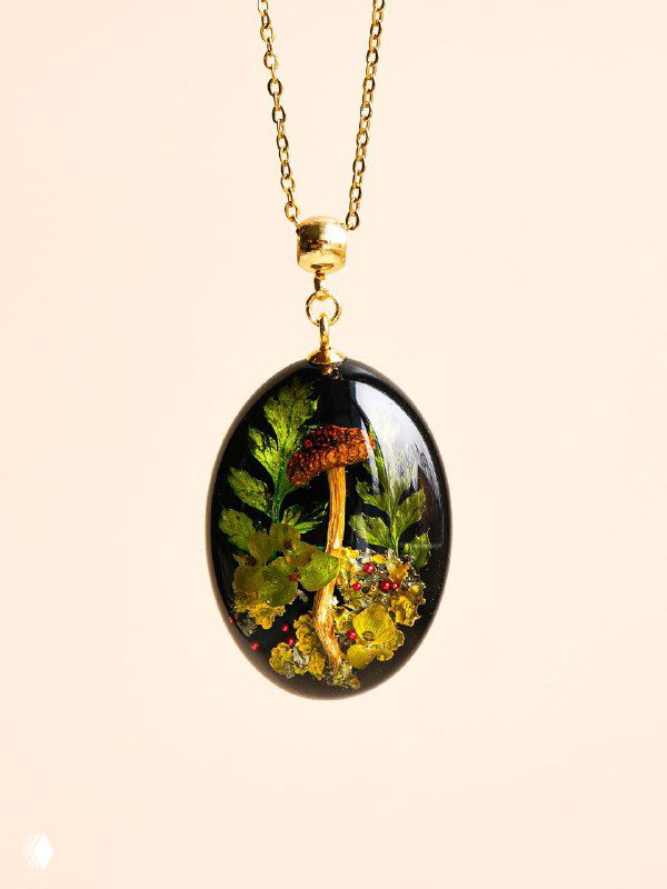 Овальный медальон на цепочке с композицией из папоротника и сухих трав, фон нейтральный, акцент на деталях и текстуре зелёных листьев.