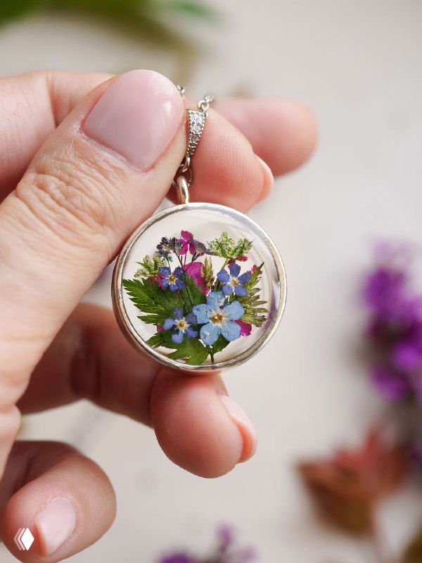 Кулон-жетон с миниатюрным букетиком из синих и фиолетовых цветков и зелёных листочков — авторская работа в руке мастера, макросъёмка.