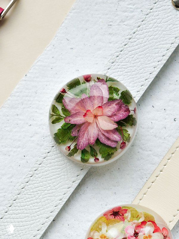 Круглый кабошон с розовым цветком и зелёными акцентами, уложенный на белый ремешок — пример украшения с акцентной зеленью в дизайне.