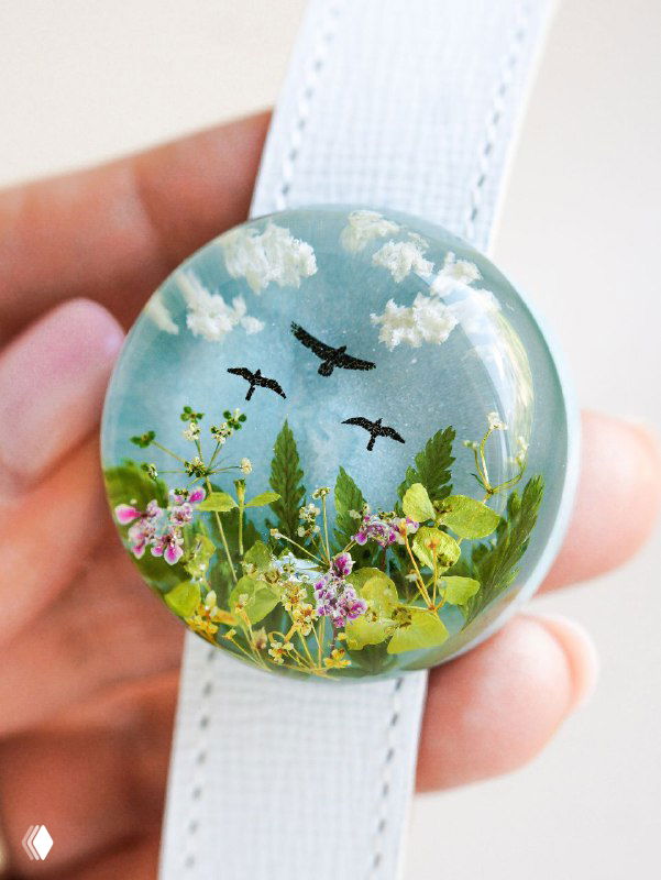 Круглый брелок с изображением мини-поля: зелень, мелкие цветки и силуэты летающих птиц — декоративный мотив с природными элементами.