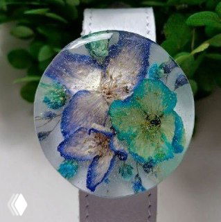 Круглый кабошон из прозрачной смолы с сухоцветами и переливами цвета; видно строение смолы, лепестки, блики и возможные мелкие пузырьки.