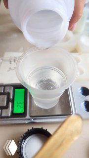 Отмеривание и переливание смолы в пластиковый стакан на электронных весах; видна мерная посуда, деревянная палочка и крышка молда.