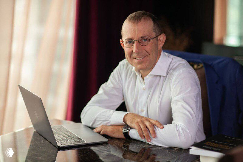 Портрет делового мужчины за ноутбуком в офисе, улыбающийся, демонстрирует атмосферу деловой беседы и переговоров.