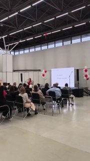 Зал с выступающими и аудиторией: сцена, экран и сидящие слушатели на форуме для самозанятых, общий план мероприятия и пространства.