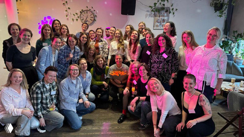 Групповое фото примерно тридцати женщин в помещении: встреча или мастерская, улыбки и дружественная профессиональная атмосфера.