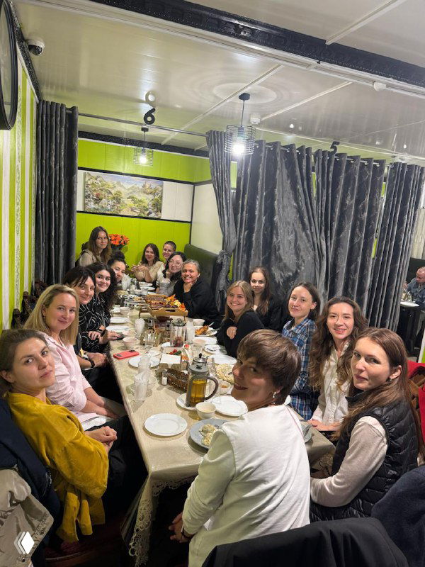 Женщины за длинным столом во время ужина: тарелки и напитки, беседа, неформальное общение и элементы нетворкинга.