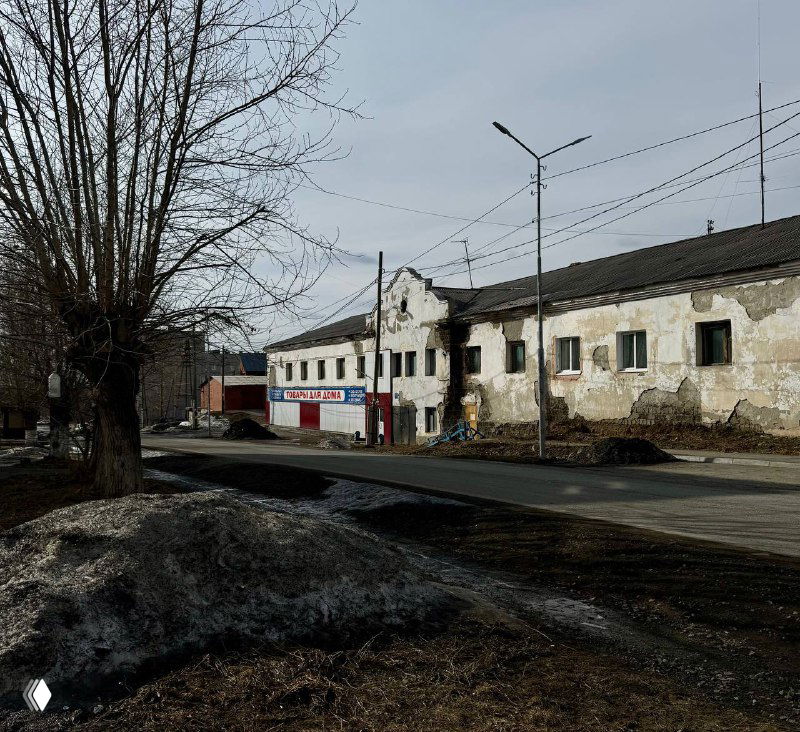 Старая городская улица в Карпинске: обветшалые дома, тающие сугробы и голые деревья весной, пустынный вид без активного движения.