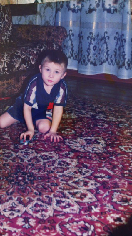 Маленький ребёнок ползает по узорчатому ковру в комнате, играет с игрушечной машинкой на бытовом снимке из детства.