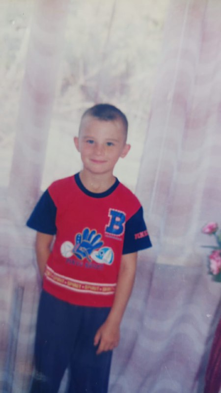 Типичная студийная фотография мальчика в футболке с буквой «B» на фоне занавесок, портрет школьного возраста из семейного архива.