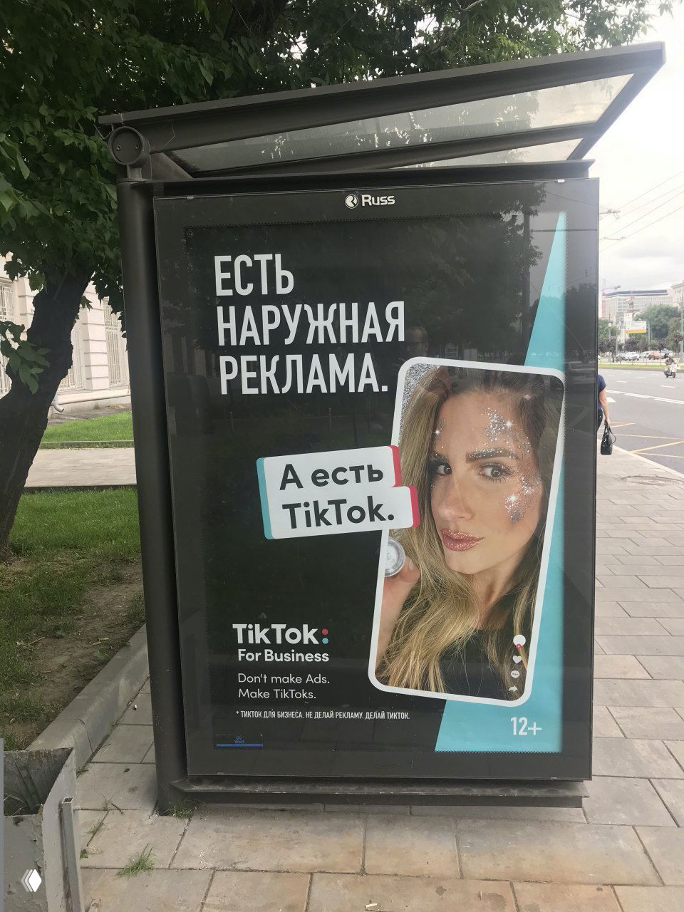 Уличный постер кампании TikTok с текстом «Есть наружная реклама. А есть TikTok», изображением девушки в рамке и фирменными элементами бренда.
