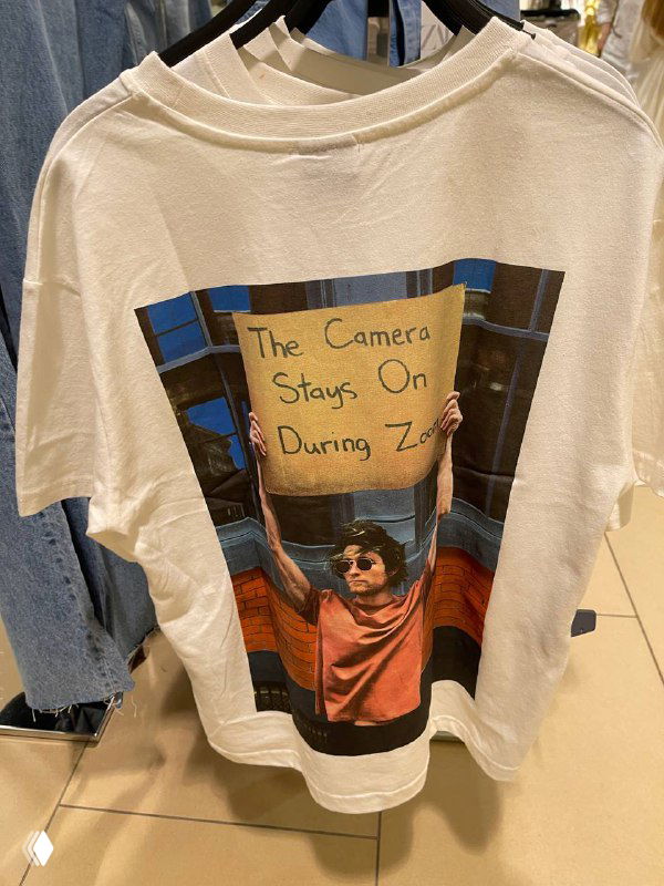 Футболка с печатью: фотография парня, держащего картонную табличку в руках — пример мем-культуры на полке магазина Zara в витрине