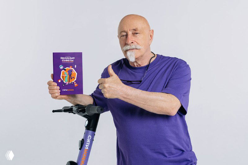Григорий Остер держит книгу «Вредные советы», показывает на издание большим пальцем; рядом стоит самокат на нейтральном фоне.