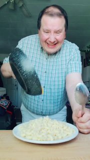 Мужчина в кадре наливает сыр на отваренные макароны, широкая улыбка — кадр из вирусного видео, давящий на абсурдную комичность тренда в TikTok.