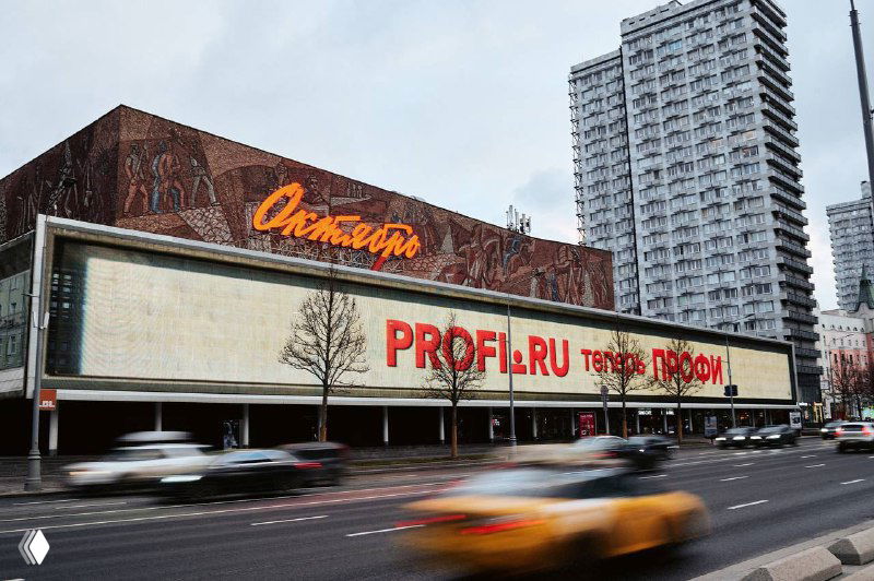 Фасад здания на Арбате с крупных форматом графикой Profi.ru, красные буквы рекламы на стене и движение автомобилей на переднем плане.