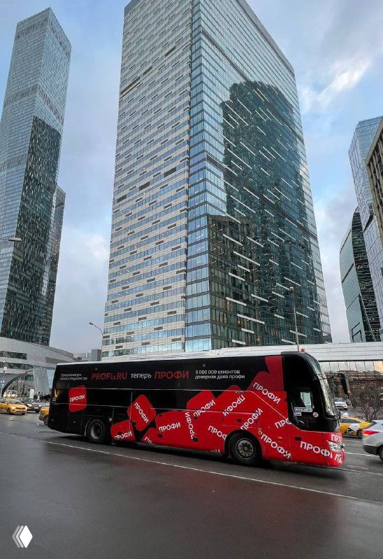 Красный брендированный автобус с повторяющимся логотипом «Профи» на фоне стеклянных высоток Москва-Сити, демонстрирующий уличную кампанию бренда.