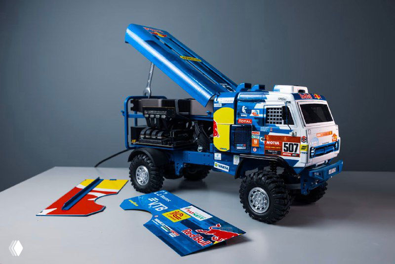 Игровой ПК в фирменной ливрее RedBull и КАМАЗ‑мастер с открытым кузовом; корпус содержит элементы реального грузовика, прошедшего Дакар, на нейтральном фоне.
