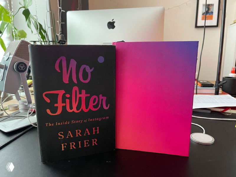 На столе две книги: на переднем плане — «No Filter» Сары Фраер, рядом яркая градиентная обложка; рабочее место с монитором на заднем плане.