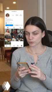 Женщина сидит за столом и смотрит в смартфон; на фоне видно интерфейс соцсети с профилем и публикациями, кадр иллюстрирует переписку/интерфейс.