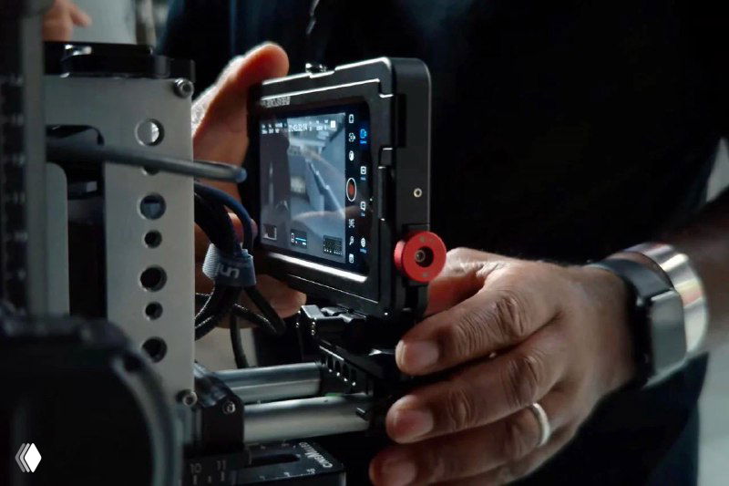 Руки оператора на профессиональном мониторе и риге, видно экран и элементы управления — кадр со съёмочной площадки, иллюстрирующий работу техники.