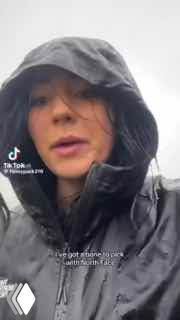 Крупный план девушки в капюшоне и промокшей куртке The North Face под дождём; видны капли воды на ткани, логотип и водяной знак TikTok.