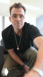 Человек в очках делает вертикальное селфи в интерьере офиса; кадр показывает торс и лицо в полуразвороте, иллюстрация темы Reels и репостов