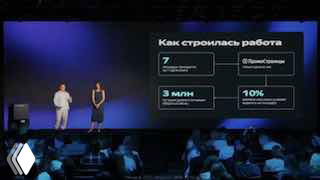 Фотография конференции: двое выступающих на сцене перед слайдом с графиками, цифрами и блоками, аудитория в затемнённом зале