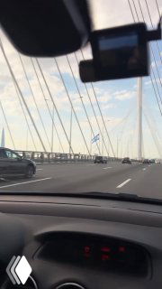 Вид из салона автомобиля на дорожное полотно и кабельный мост; приборная панель внизу кадра и трафик на дороге, контекст съёмки ролика для Буше