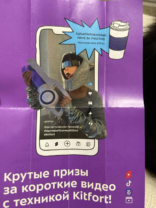 Страница вкладыша в фиолетовой гамме с иллюстрацией телефона и промоблоком: короткие видео и призы, лист сложен в руках автора снимка.