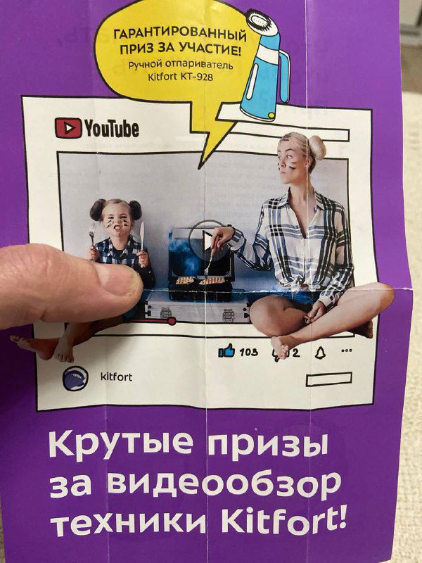 Фиолетовый вкладыш с макетом YouTube-плеера и подписью о гарантированном призе за участие; видна часть дизайна и рук держателя.