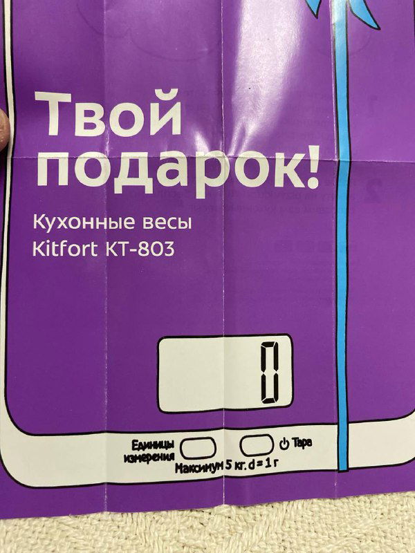 Фрагмент вкладыша с крупным заголовком «Твой подарок!» и изображением кухонных весов Kitfort KT-803 на фоне фиолетового фона.