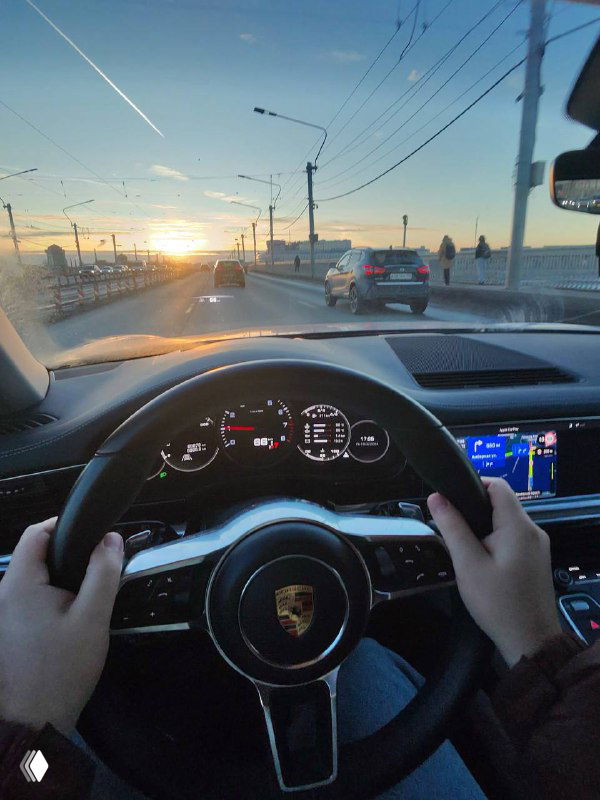 Ещё один POV-кадр за рулём: руки на руле, мост, встречные машины и низкое солнце на горизонте в городской среде.