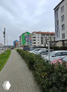 Городская улица с многоэтажками и раскрашенным фасадом; кадр снят глазами при прогулке по тротуару и показывает урбанистический фон.